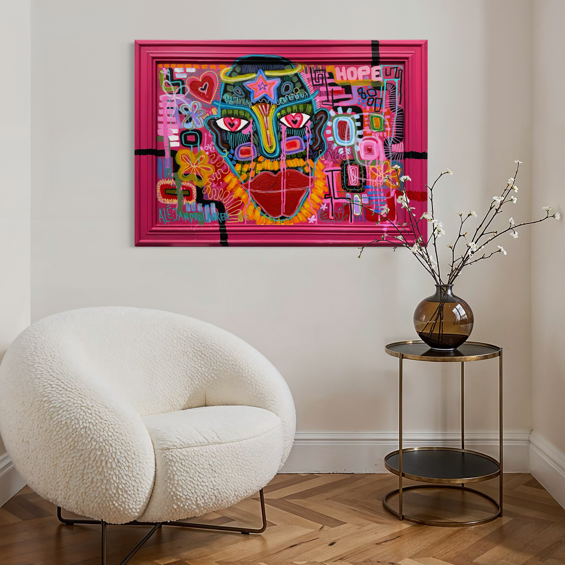 Colorful abstract painting in a bright pink frame on a wall above a white armchair.